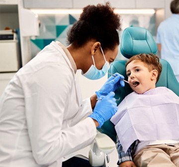 Pediatric dentist examining child's teeth with dental mirror