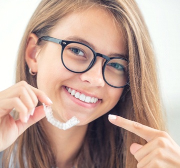 Teen smiling and pointing to Invisalign tray in Nashua