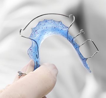 Hand holding up a blue retainer oral appliance