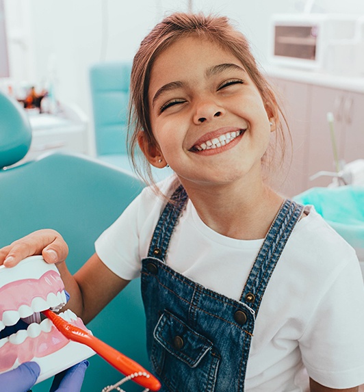 Smiling young girl practicing tooth brushing on smile model