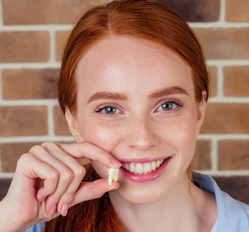 Young woman holding up tooth after extraction