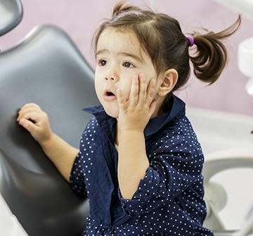 Toddler holding cheek before emergency kid's dentistry