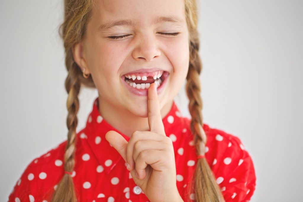 Smiling child pointing to missing tooth