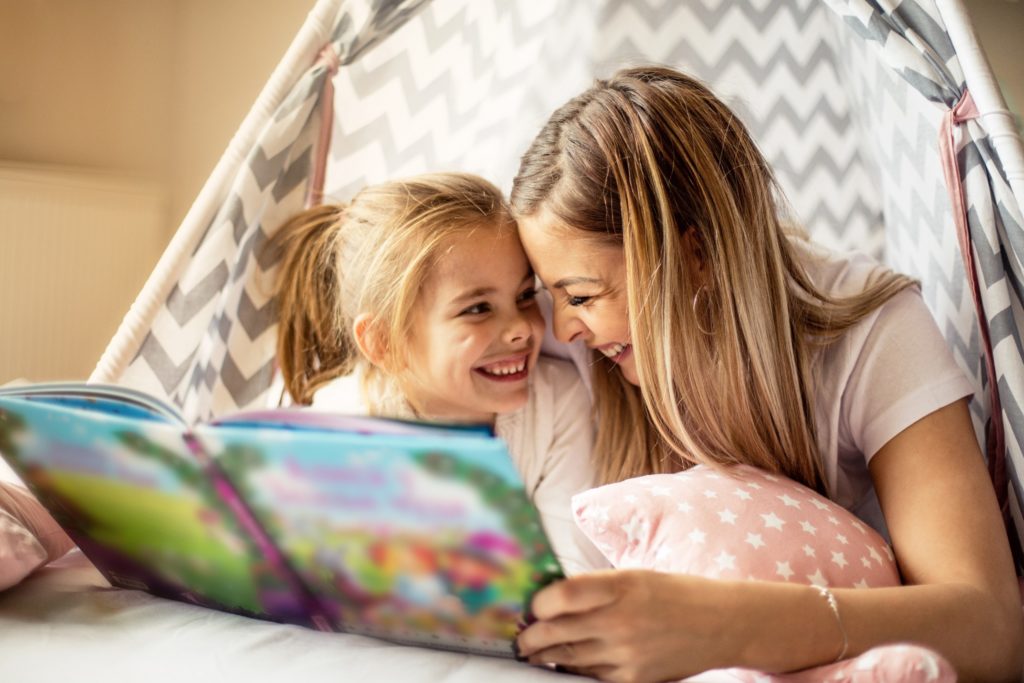 Mom and daughter reading book together in fort